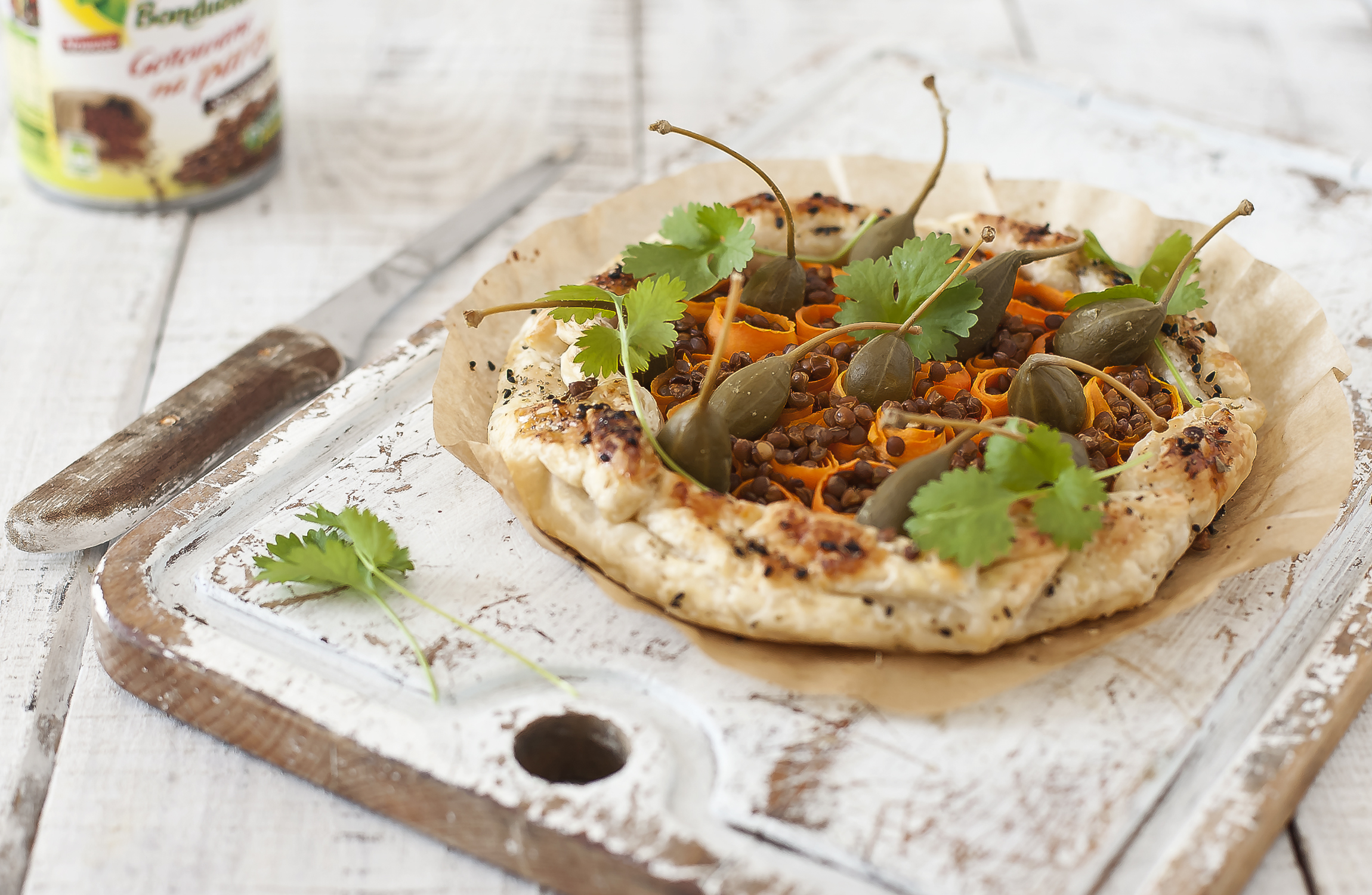 Dzisiejszy przepis: domowa tarta z soczewicą, kaparami i marchewką, podana na drewnianej desce.